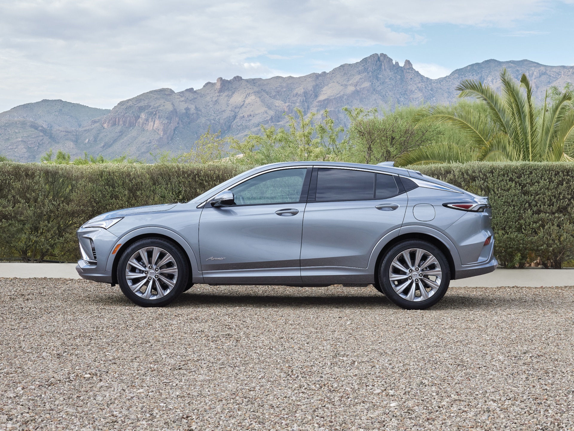 A Light Blue Buick Envista SUV Parked on a Gravel Driveway With Mountains and Desert Landscaping in the Background