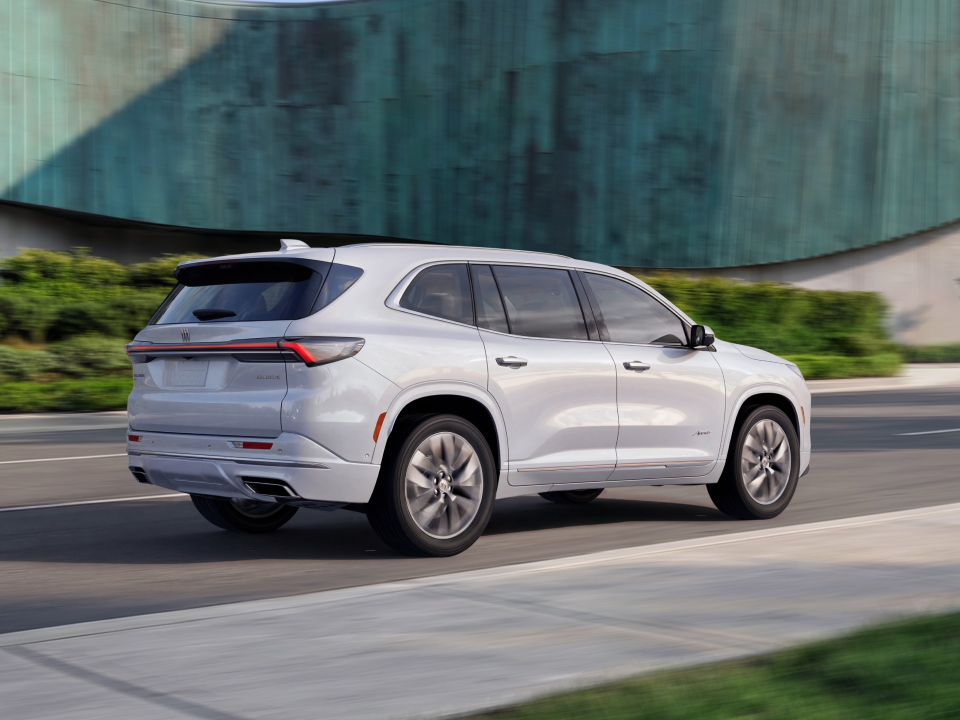 A White Buick Avenir SUV Driving Down the Road from a Rear Three Quarter View with a Modern Building in the Background