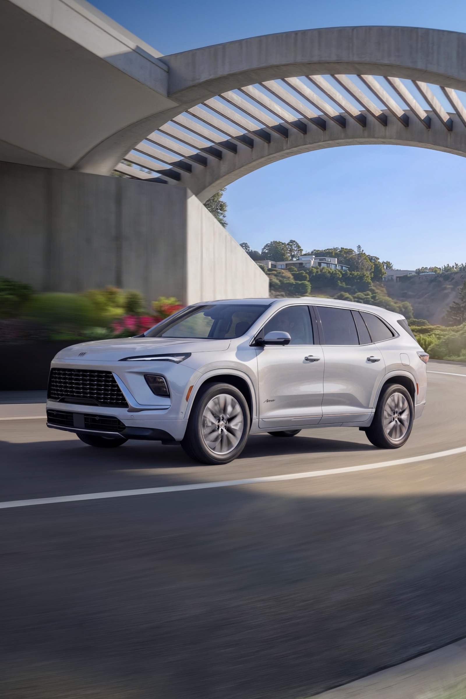 A White Buick Enclave Avenir SUV Driving Under a Concrete Overpass on a Sunny Day