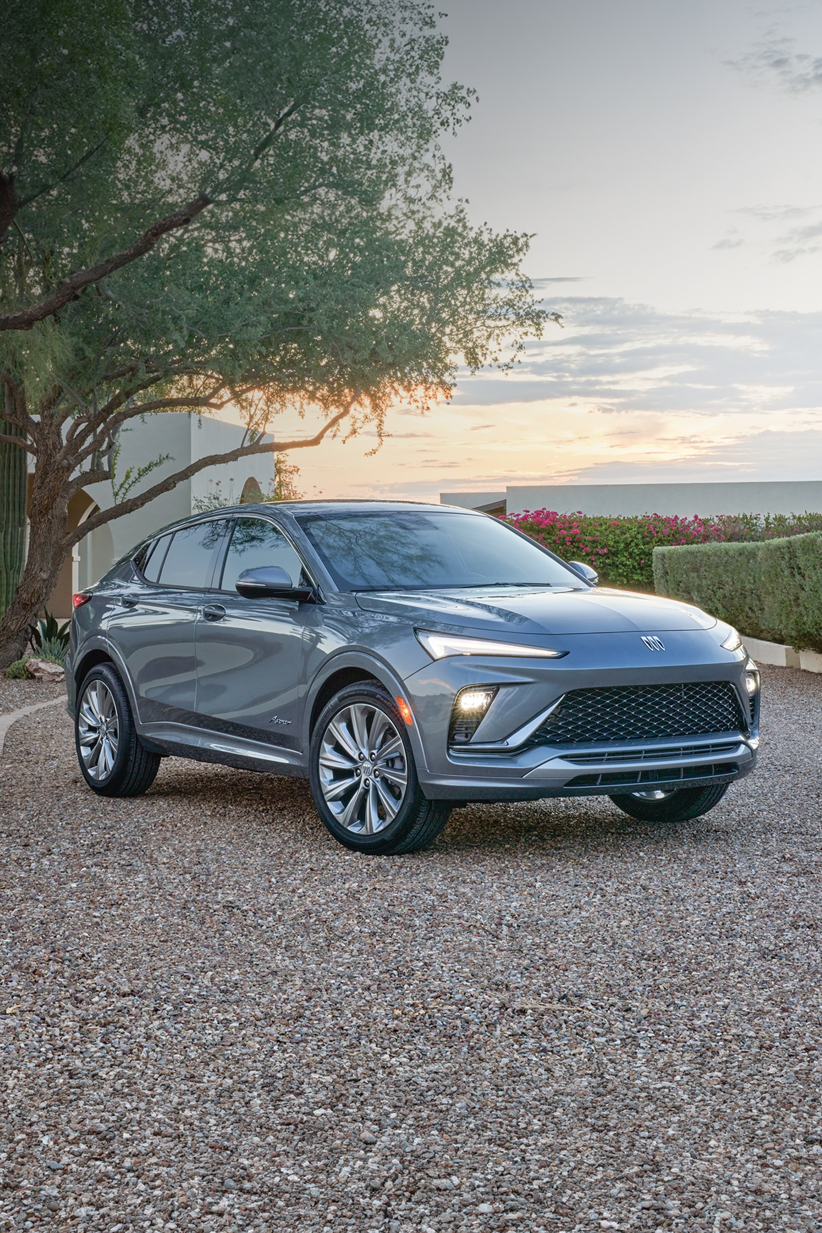 A Gray Buick Envista SUV Parked on a Gravel Driveway in a Desert Landscape at Sunset