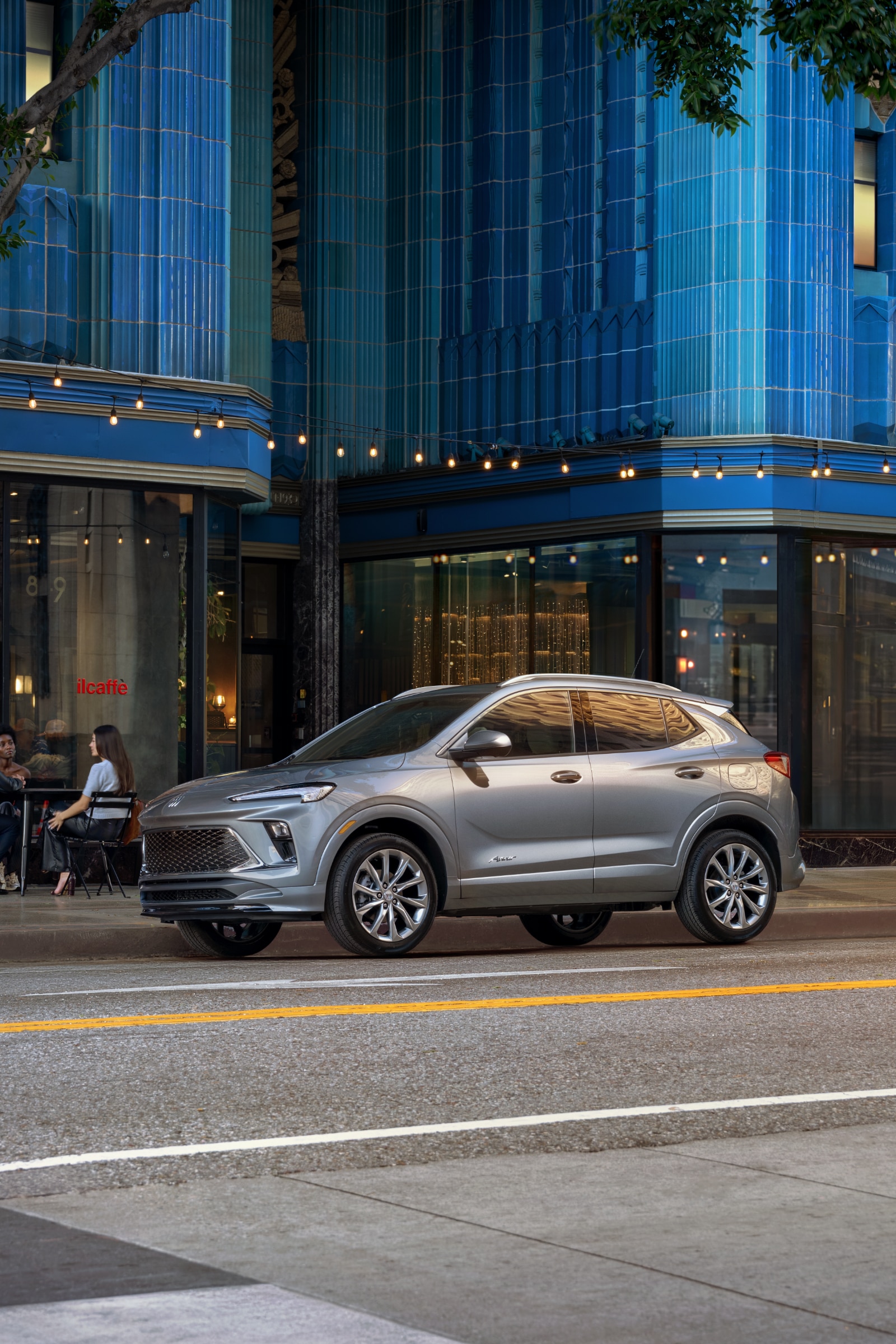 A Silver Buick Encore GX SUV Parked on a City Street in Front of a Modern Blue Building