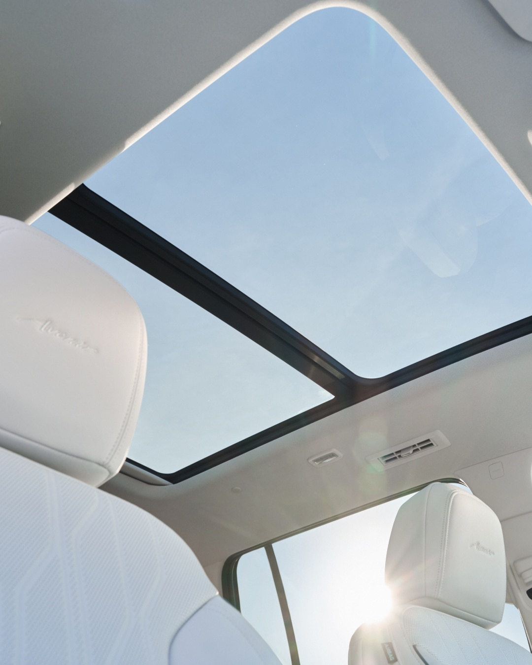 The White Interior of a Buick Enclave With a Clear View of the Panoramic Sunroof and the Bright Sky