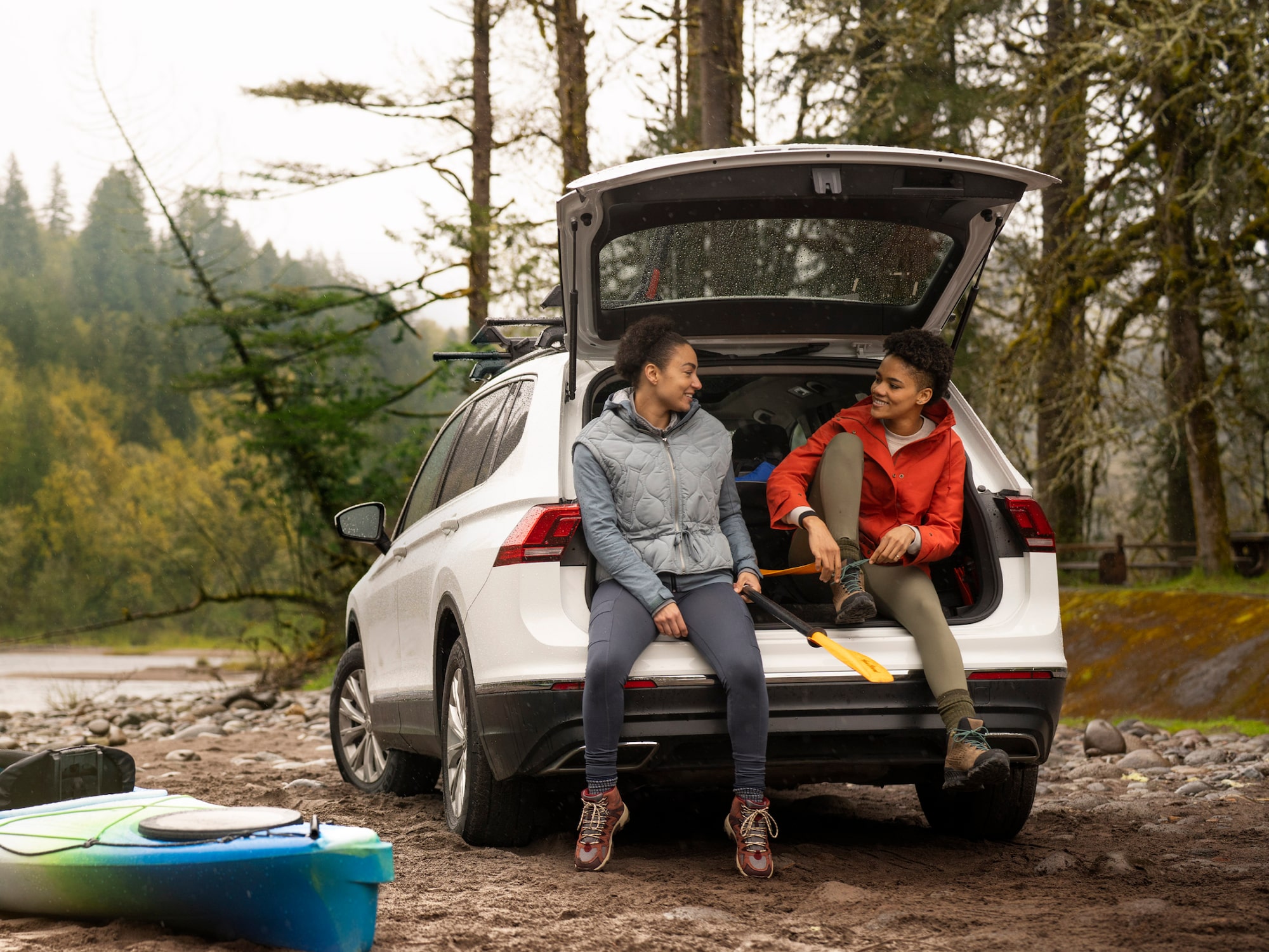 Two Friends Sitting on the Cargo Bed of a Buick SUV While Tying Their Shoes and Getting Ready for a Hike
