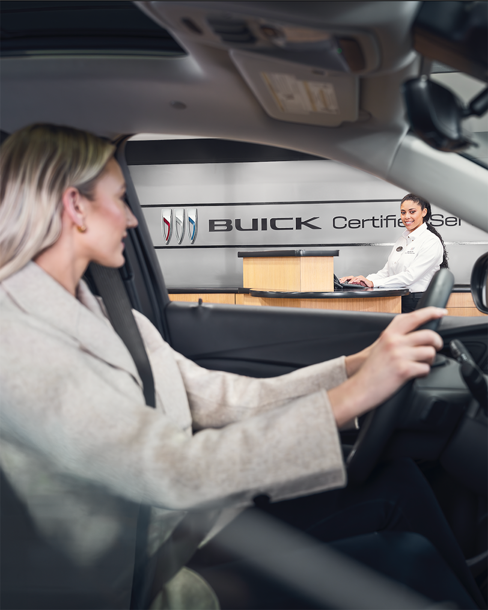 A Woman in the Driver Seat of a Vehicle, Looking at the Certified Technician Behind the Desk at a Buick Certified Service Dealership.