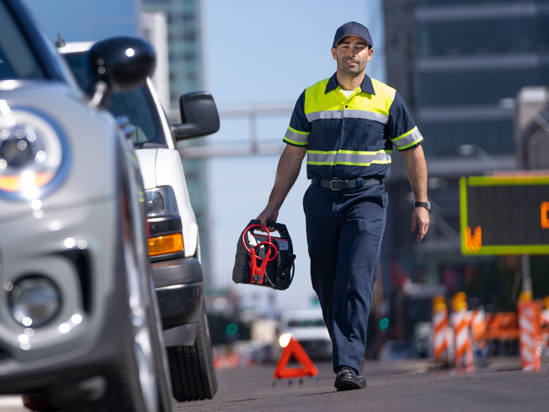 A Roadside Service Technician Walking with a Tool Bag toward a Grey Car on the Side of the Road