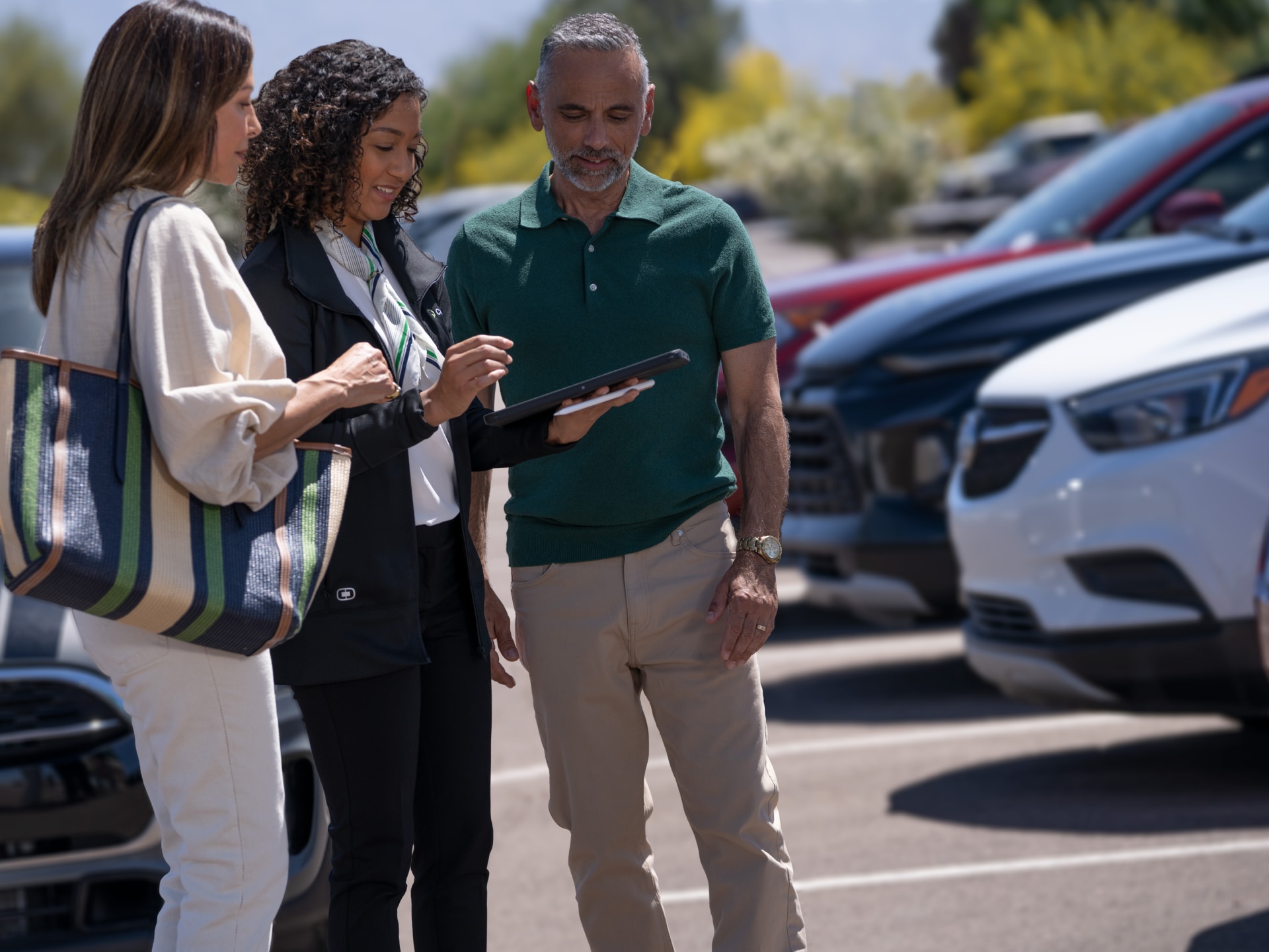 Two Customers and a Dealership Associate Looking at a Tablet in a CarBravo Lot with Certified Used Vehicles