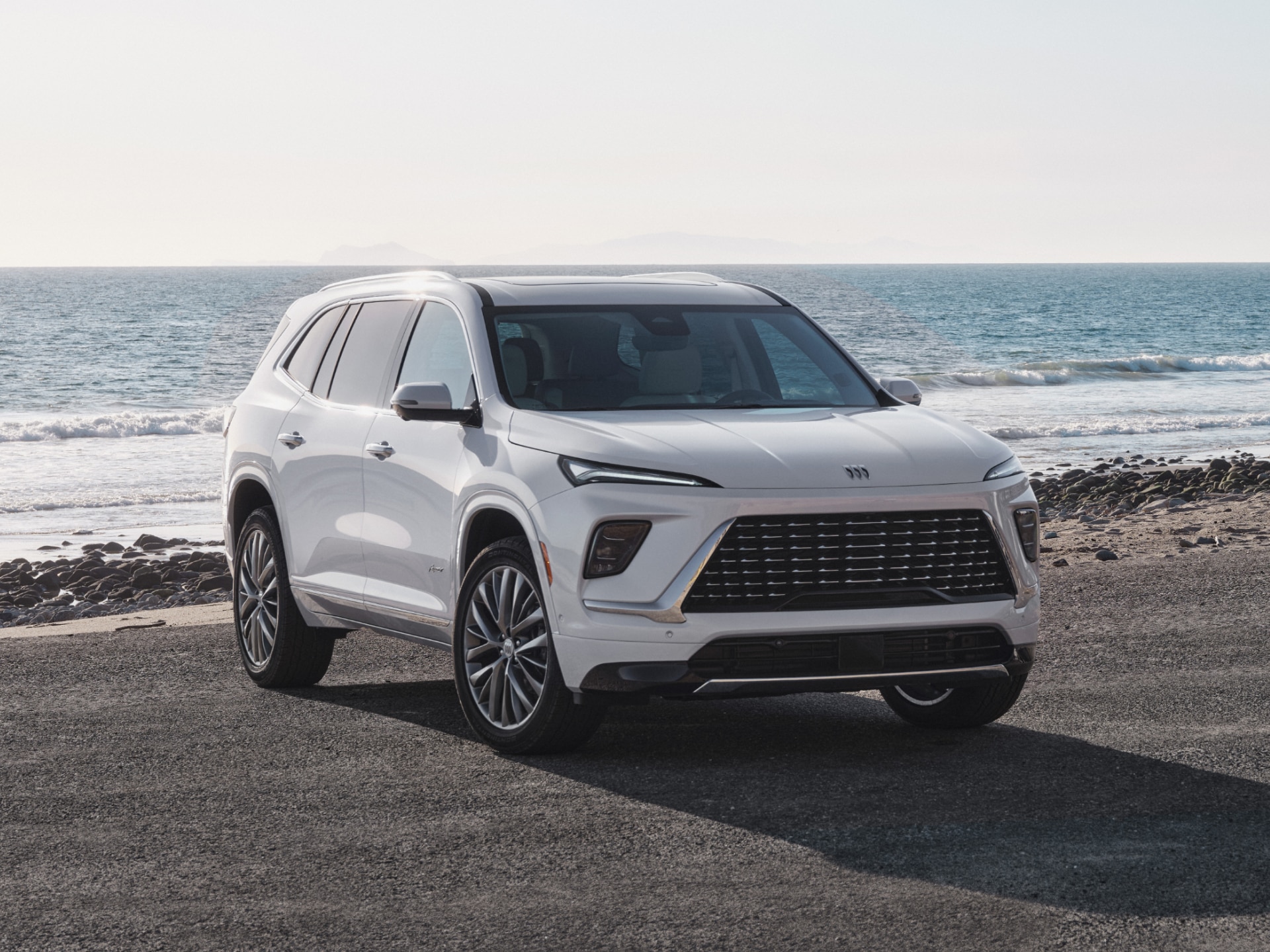 A White Buick Crossover SUV Parked on a Paved Shoreline Next to a Rocky Beach and the Ocean