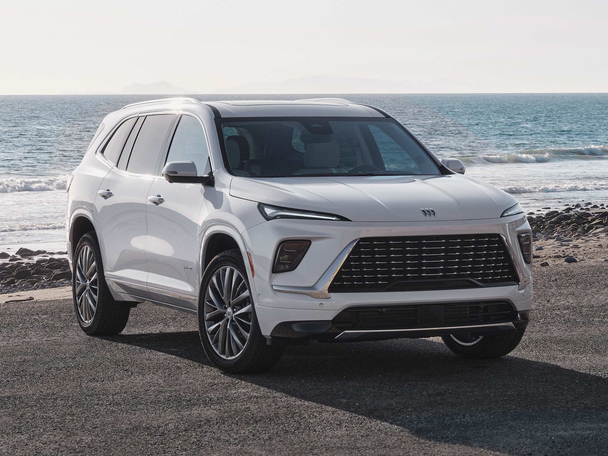 Front Three-quarters View of a White Buick Enclave Parked on a Beach as Waves Crash on the Shoreline