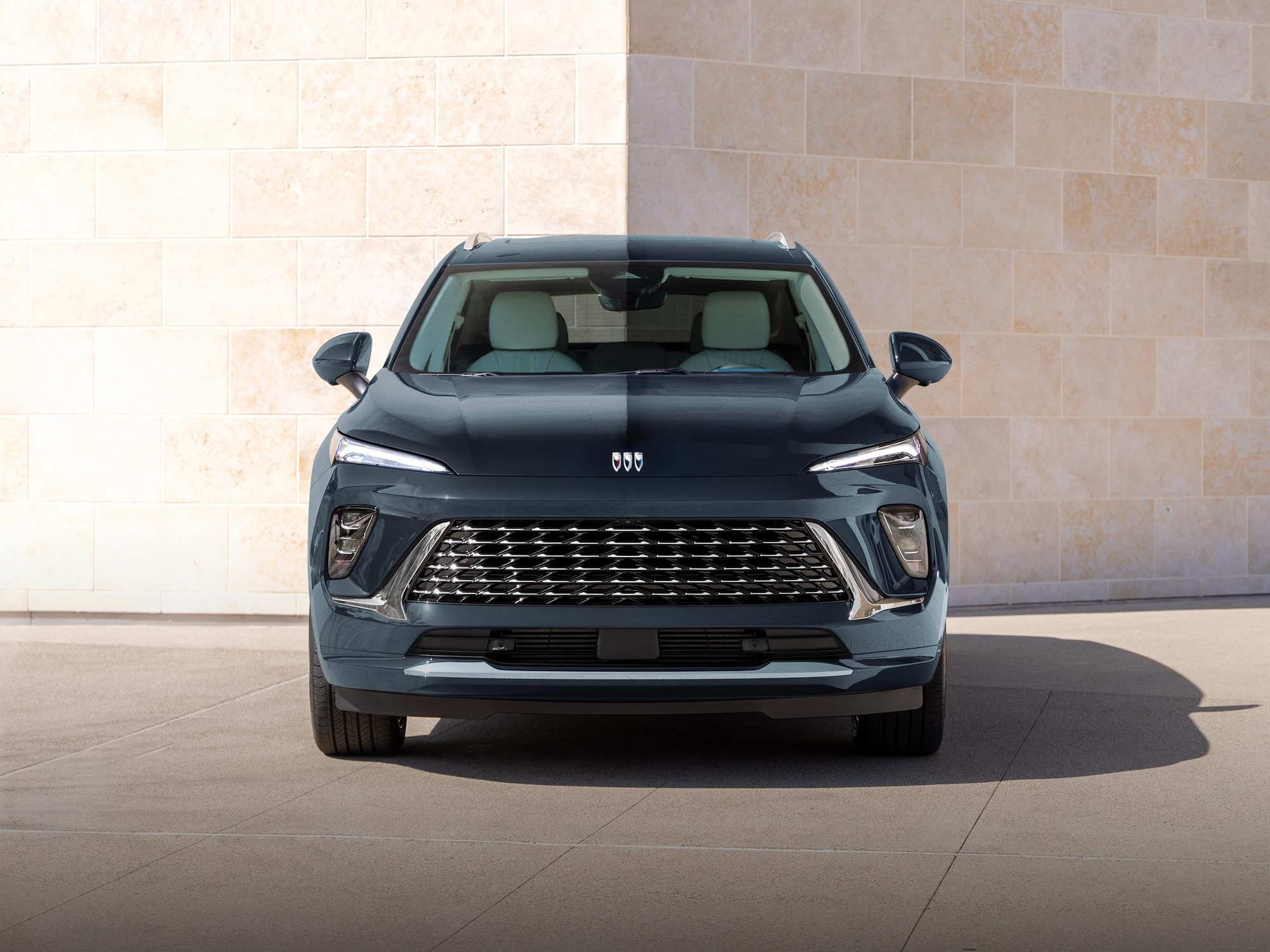 A Front View of the Dark Blue 2025 Buick Envision SUV Parked Against a Modern Stone Wall