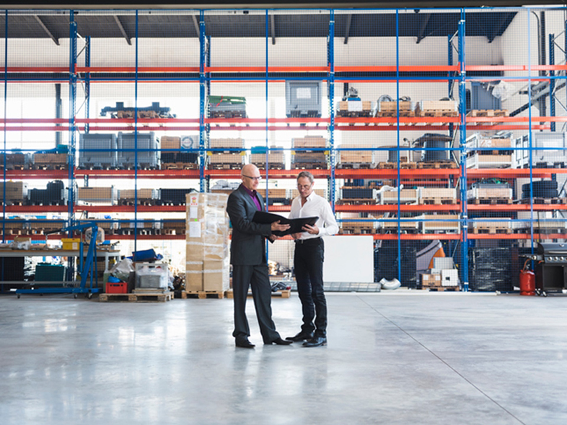 Two men holding a folder open and reviewing whilst standing in a warehouse