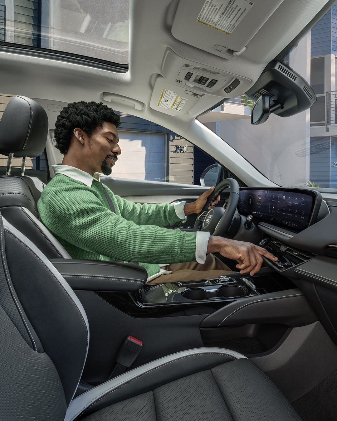 A Man in a Green Sweater Drives a Buick Featuring a Large Curved Digital Display and Black Leather Seats with Gray Accents