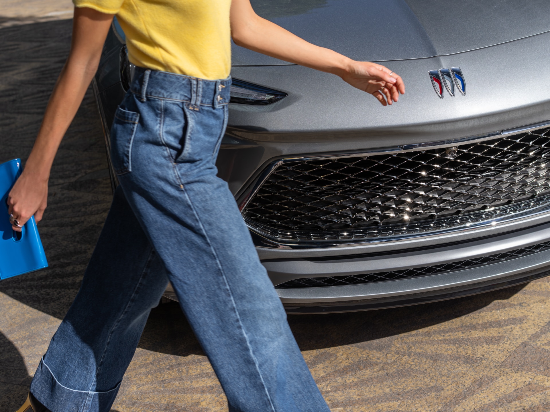 A Person Walks Past the Front of a Gray Buick Car With a Chrome Grille and the Buick Logo