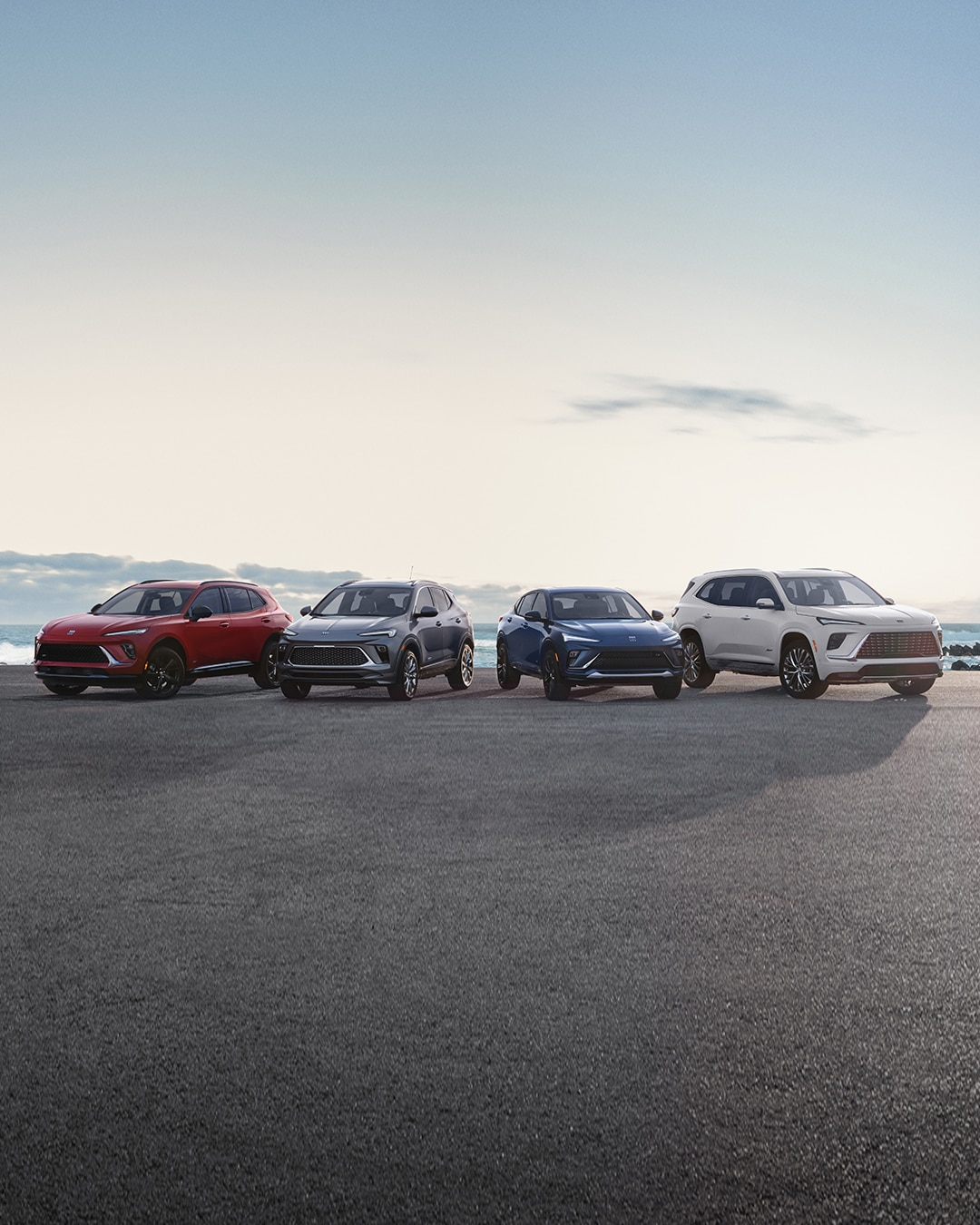 Four Buick SUVs in Red, Dark Gray, Blue, and White Parked on an Asphalt Road by the Ocean
