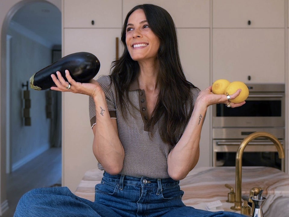 Eden Grinshpan Sitting On a Kitchen Counter Holding an Eggplant And Two Lemons