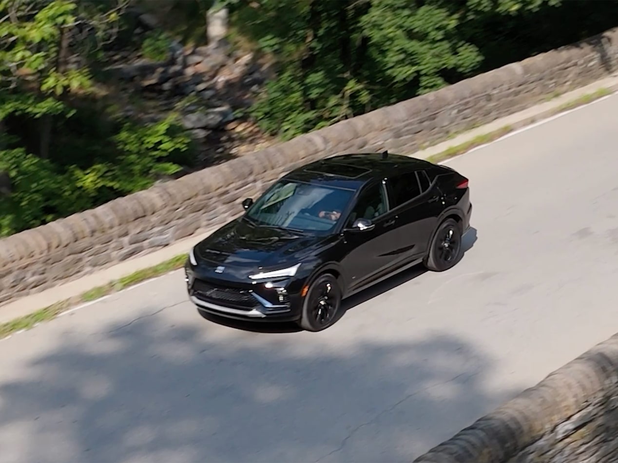 A Black Buick Envista Sport Touring Driving on a Stone Bridge Road with Green Trees