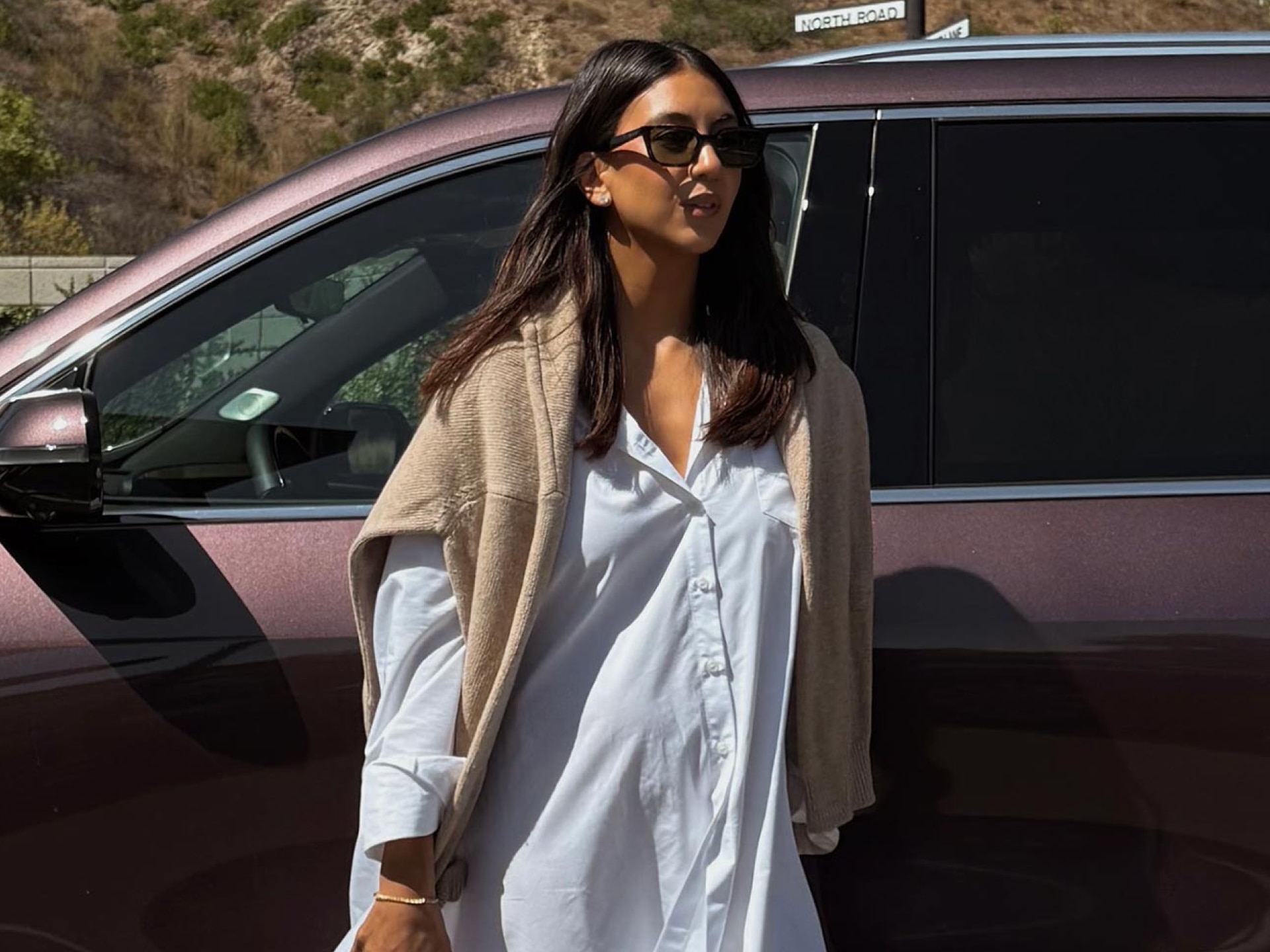 Kayla Seah Standing Alongside a Smokey Amethyst Metallic Buick Envista Wearing a White Dress and a Beige Sweater