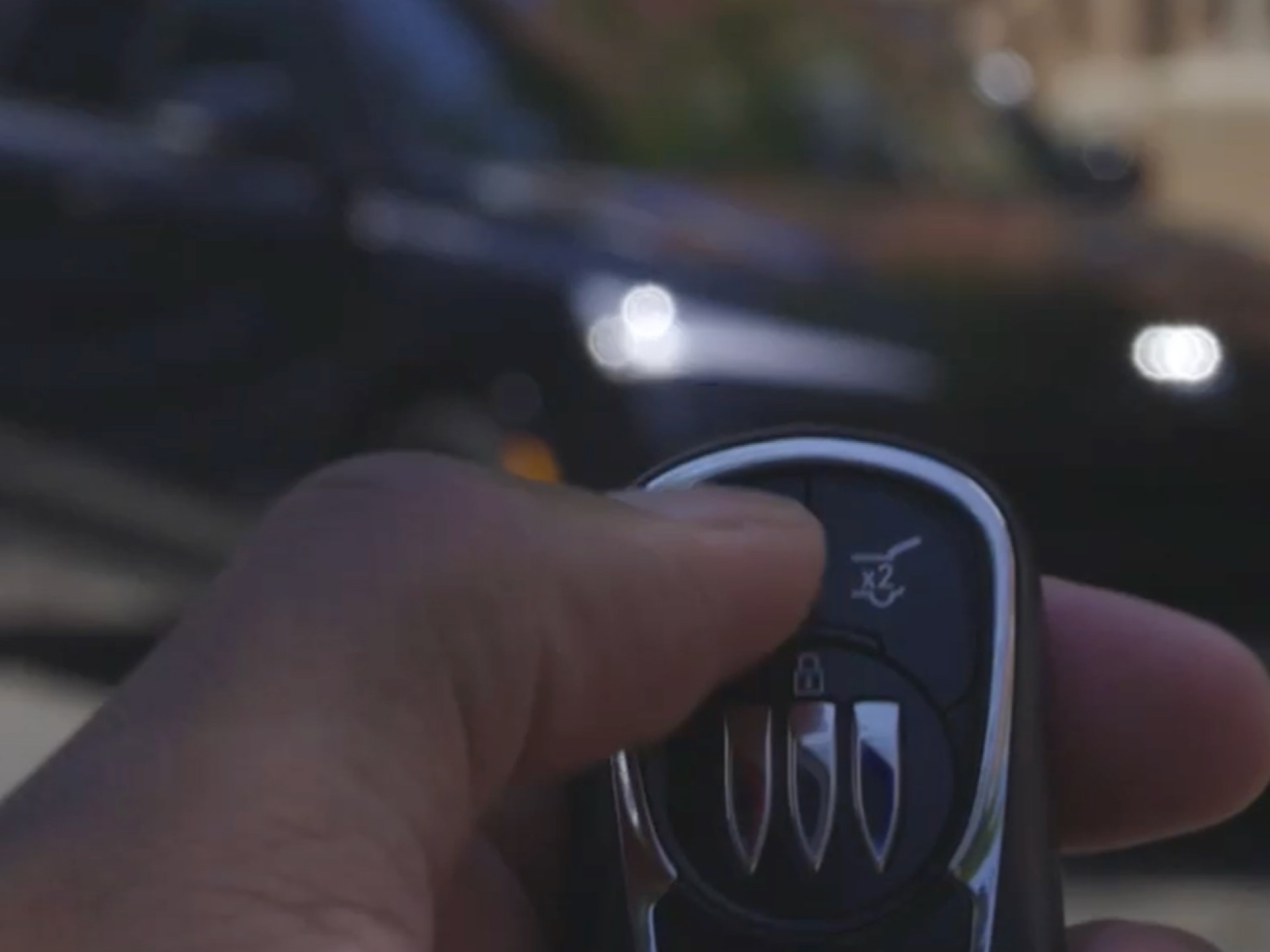 A Hand Holding a Buick Key Fob with a Blurred Black Buick Envista in the Background