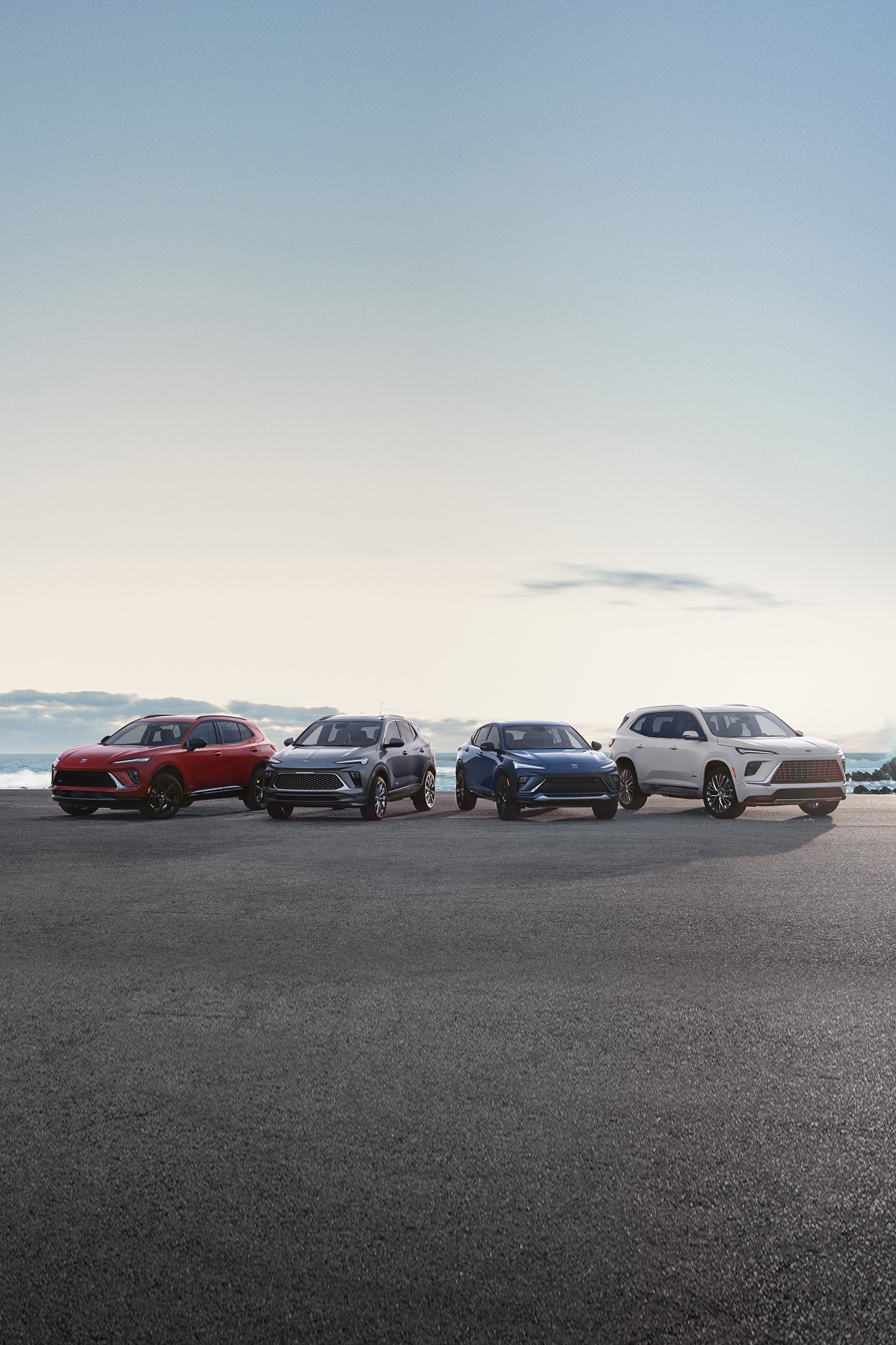 Four Buick SUVs of Different Colors Lined Up on an Asphalt Lot Next to the Ocean under a Bright Sky