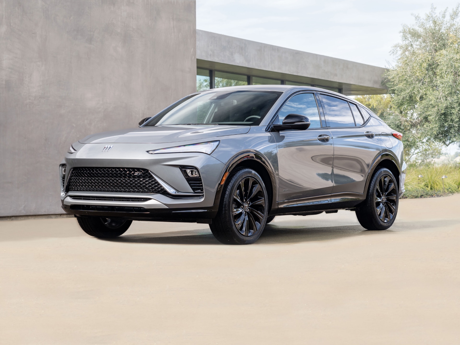 A Front Quarter View of a Sleek Gray Buick Envision Avenir SUV with Black Wheels Parked in Front of a Modern Concrete Building