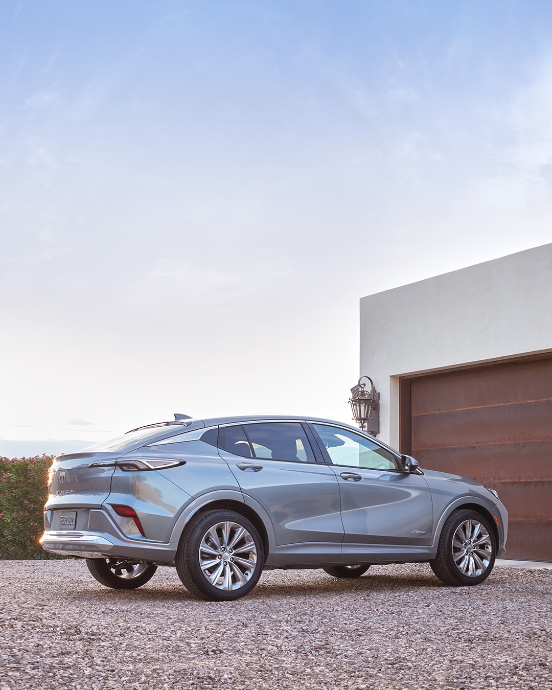 A Gray Buick Envision Avenir Parked on a Gravel Driveway with a Smiling Couple Walking Beside It a Modern House in the Background