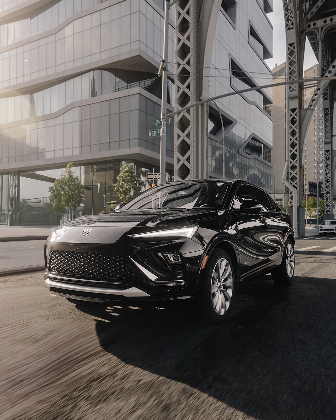 A Sleek Black Buick SUV Driving on a City Street with Modern Buildings and a Bridge in the Background