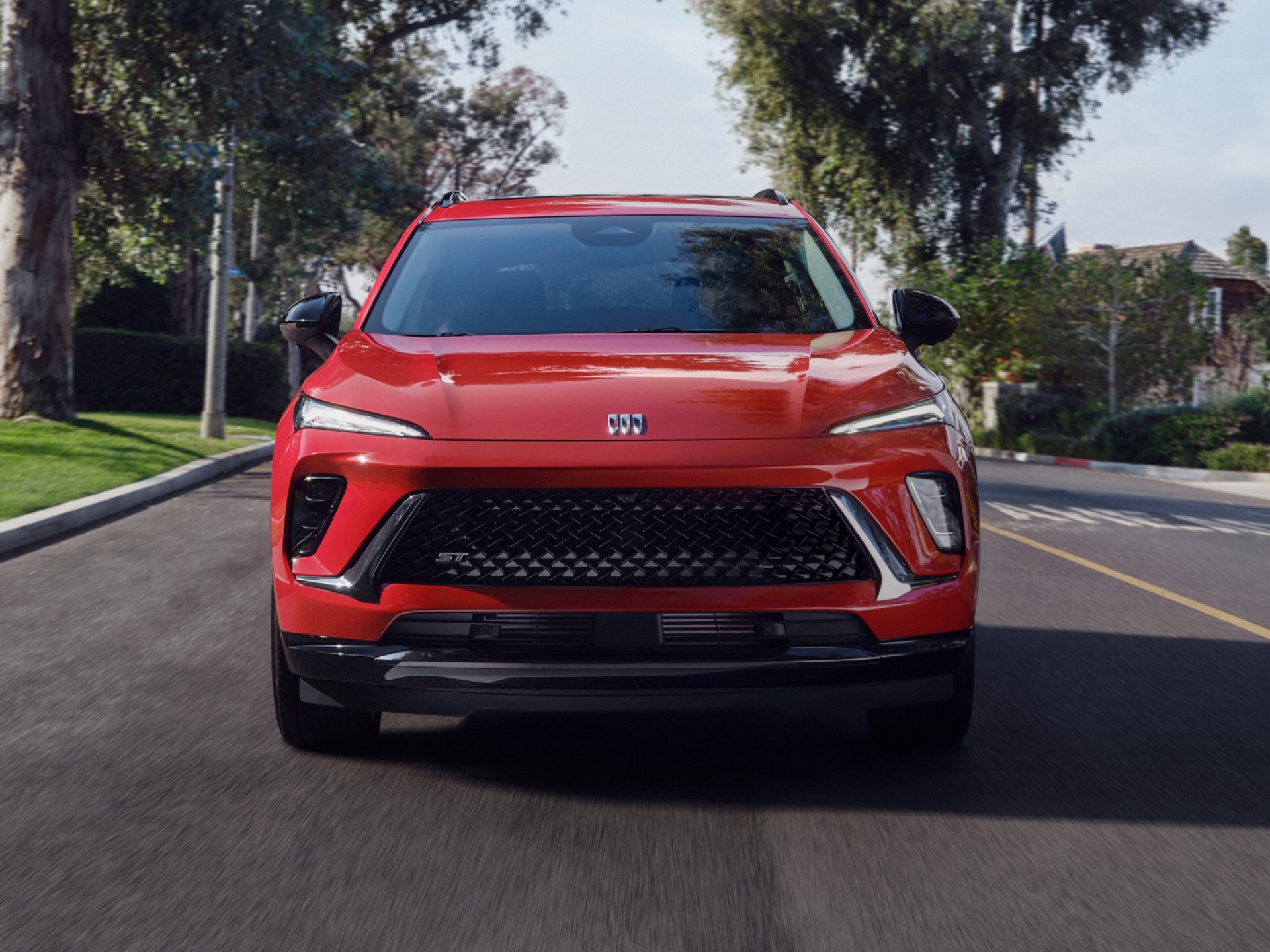 A Front View of a Bright Red Buick SUV Driving on a Tree Lined Street in a Suburban Neighborhood