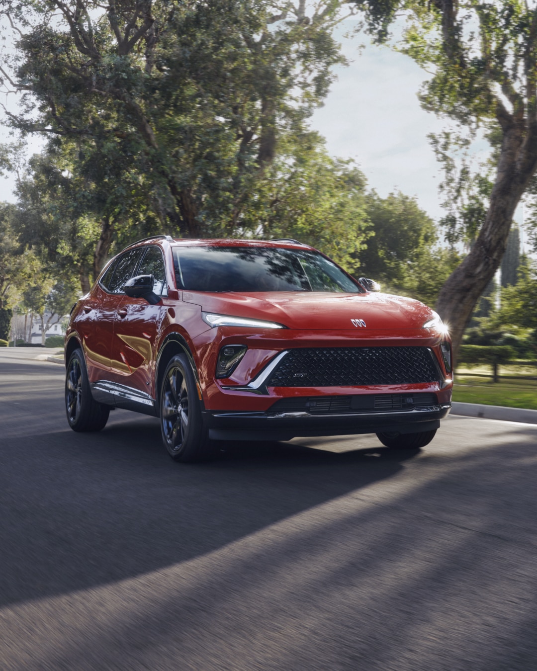 Front Three-Quarters View of a Red Buick SUV Driving Down a Neighborhood Street