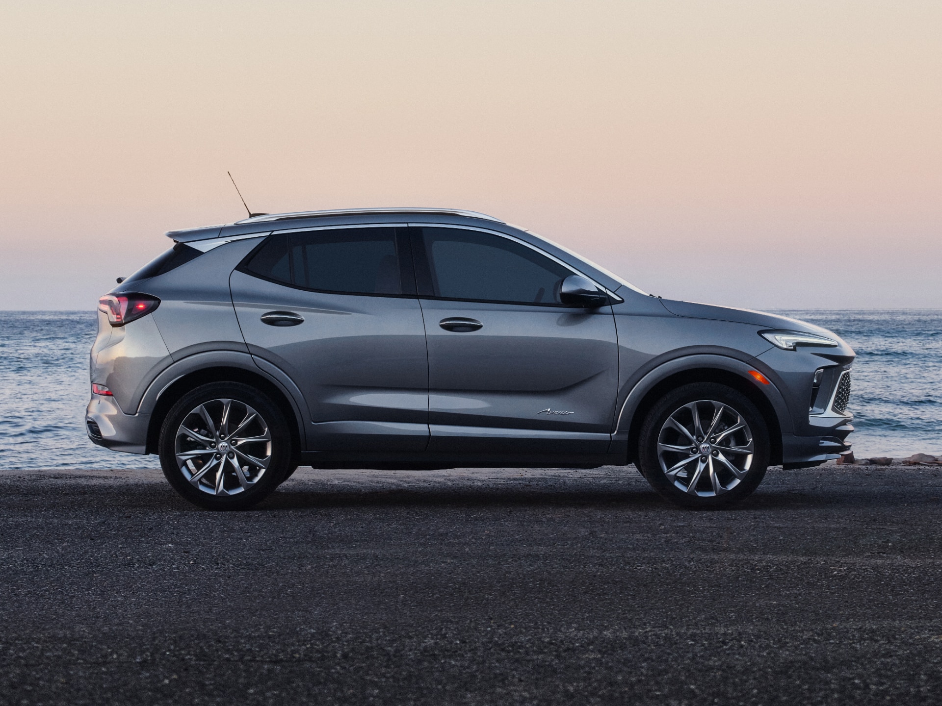 A Silver Buick Encore GX SUV Parked Sideways on a Road with the Calm Ocean at Sunset