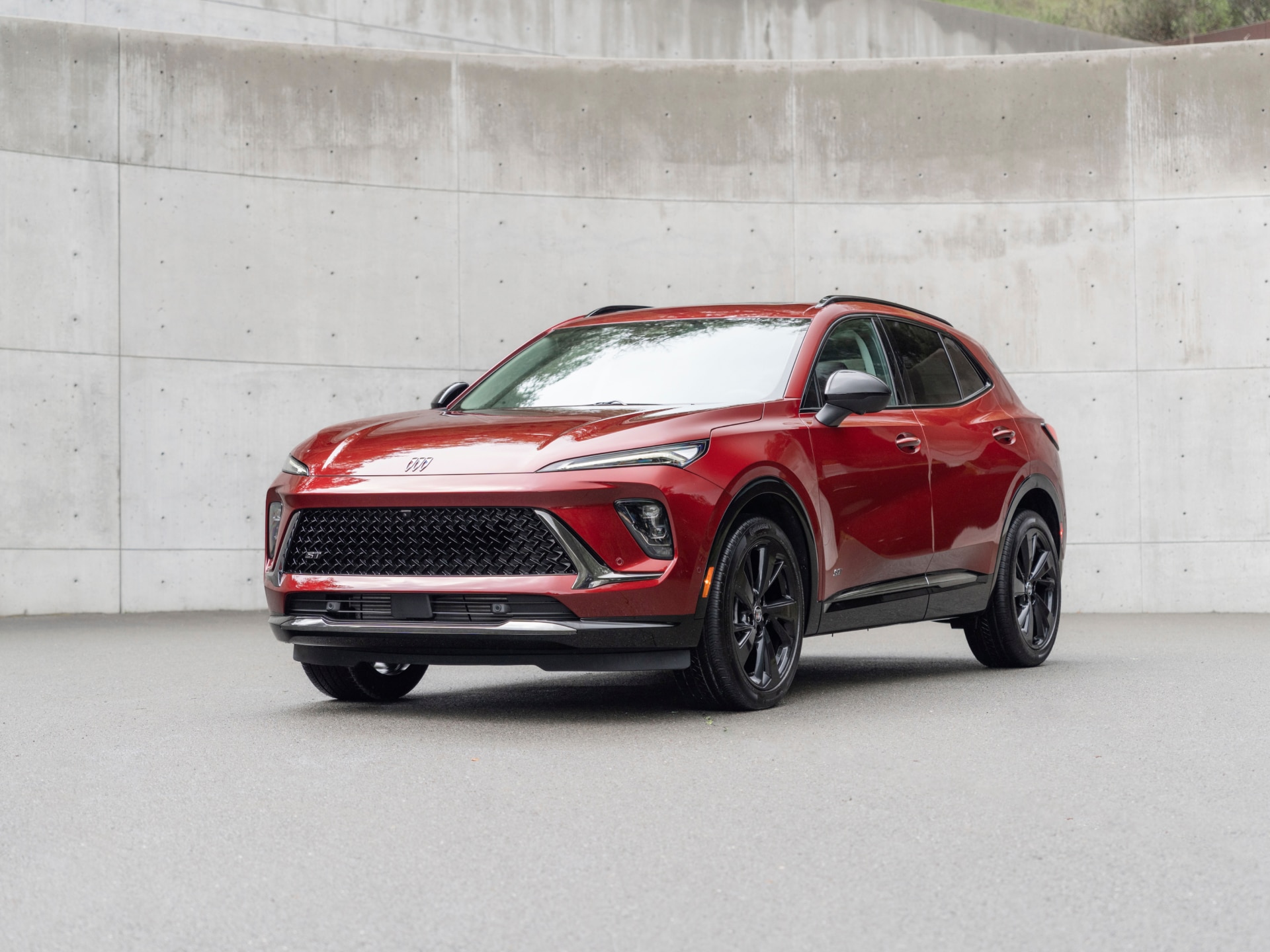 A Deep Red Buick Envista ST Parked on a Dark Gray Surface in Front of a Textured Concrete Wall