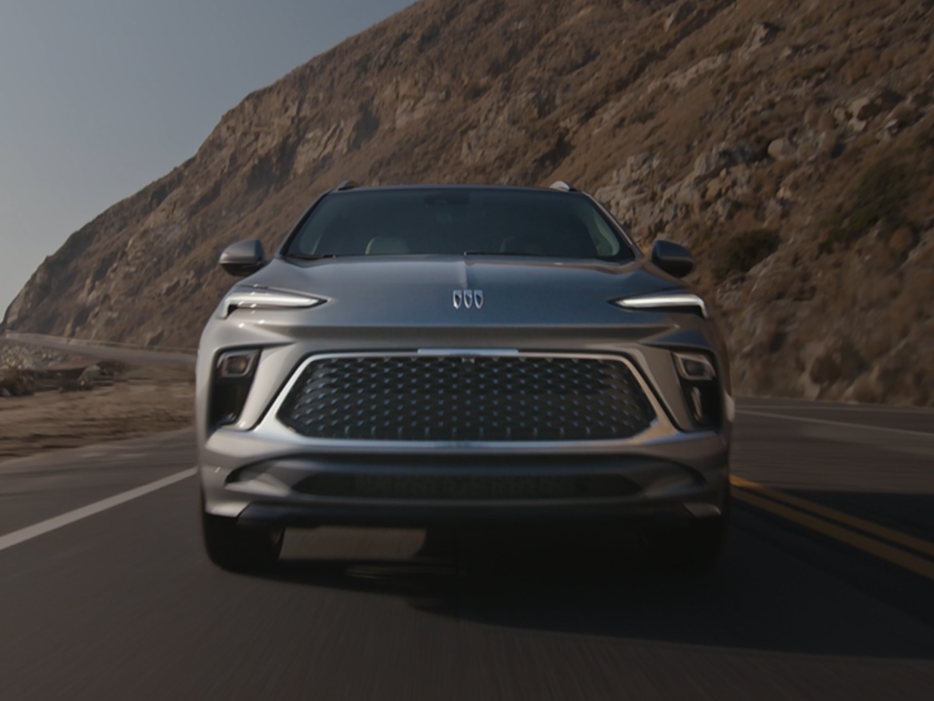 A gray Buick Encore GX driving on a winding road along a rocky coastline.
