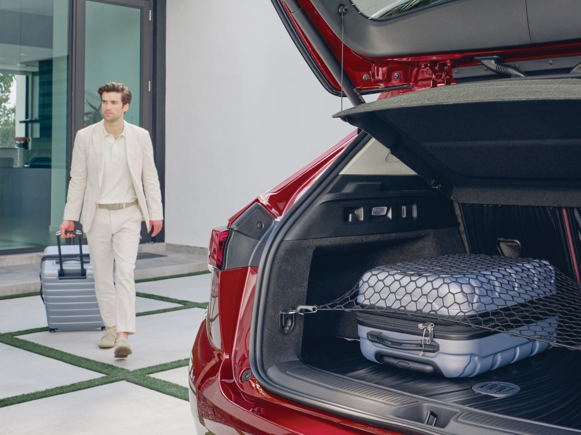 A Man Walking with his Luggage to the Opened Liftgate of a Buick Envision with a Cargo Net and Integrated Cargo Liner Accessory