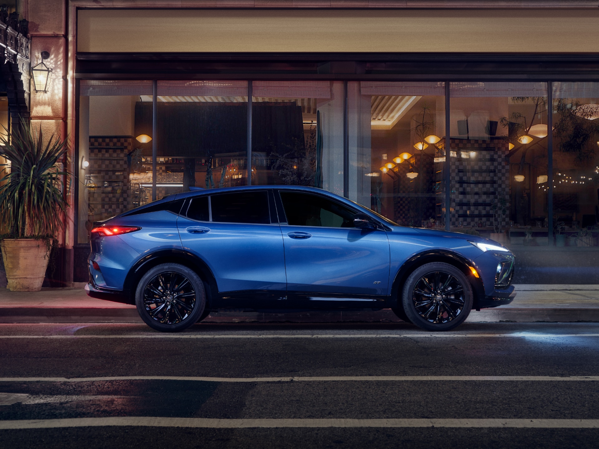 A Blue Buick Envista ST Parked on a City Street at Night with Building Lights