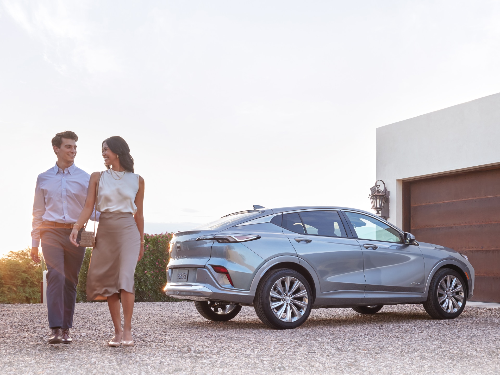 A Gray Buick Envision Avenir Parked on a Gravel Driveway with a Smiling Couple Walking Beside It a Modern House in the Background