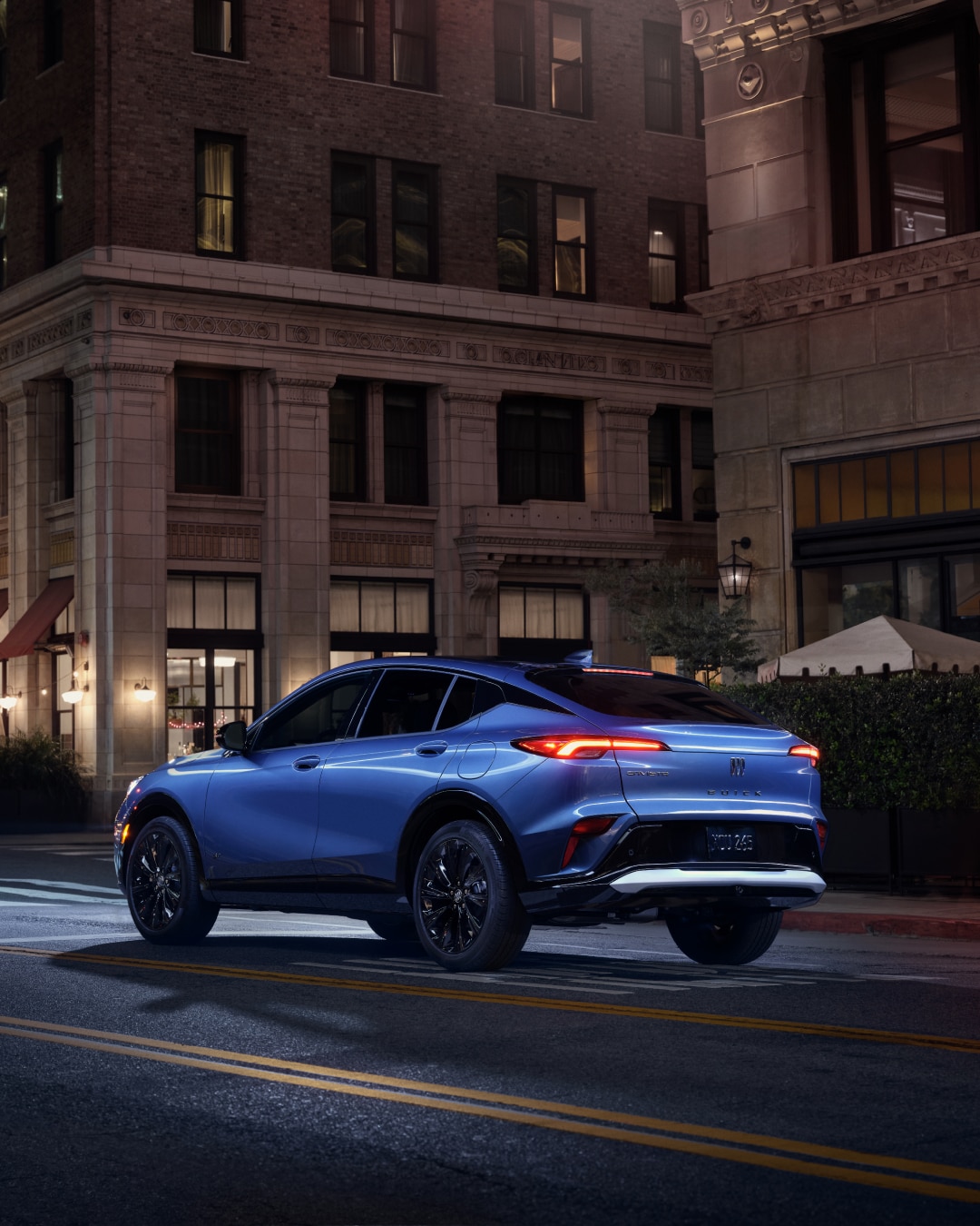 A Blue Buick SUV Parked on a City Street at Night with Taillights Illuminated and the Buick Logo Visible