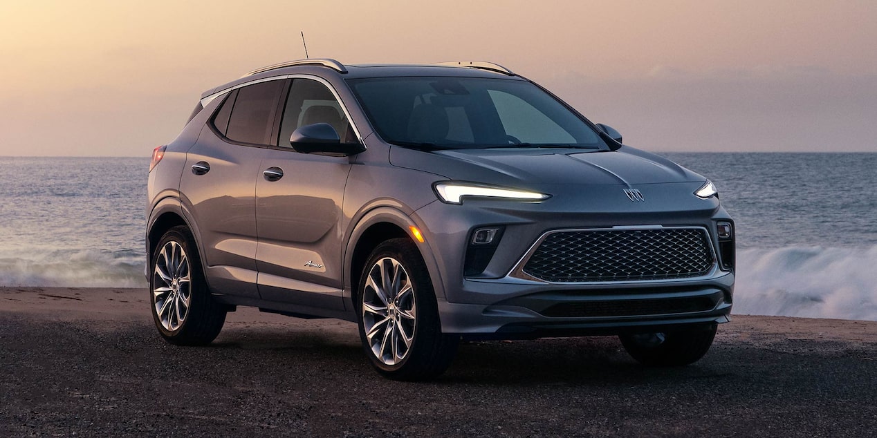 A Gray Buick Encore GX SUV Parked On The Asphalt Road By The Ocean At Sunset 