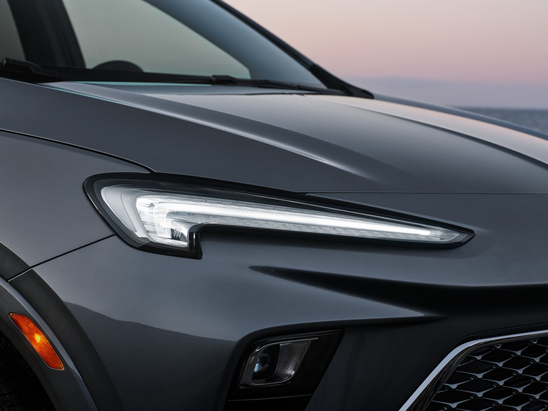 A Three-Quarters Front View of a Gray Buick SUV’s Headlight, Shown at Sunset.