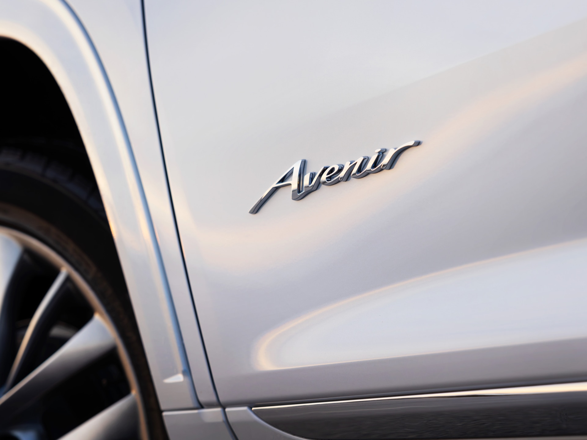A White Buick Avenir’s Side Door Emblem and a Partial View of the Front Wheel.
