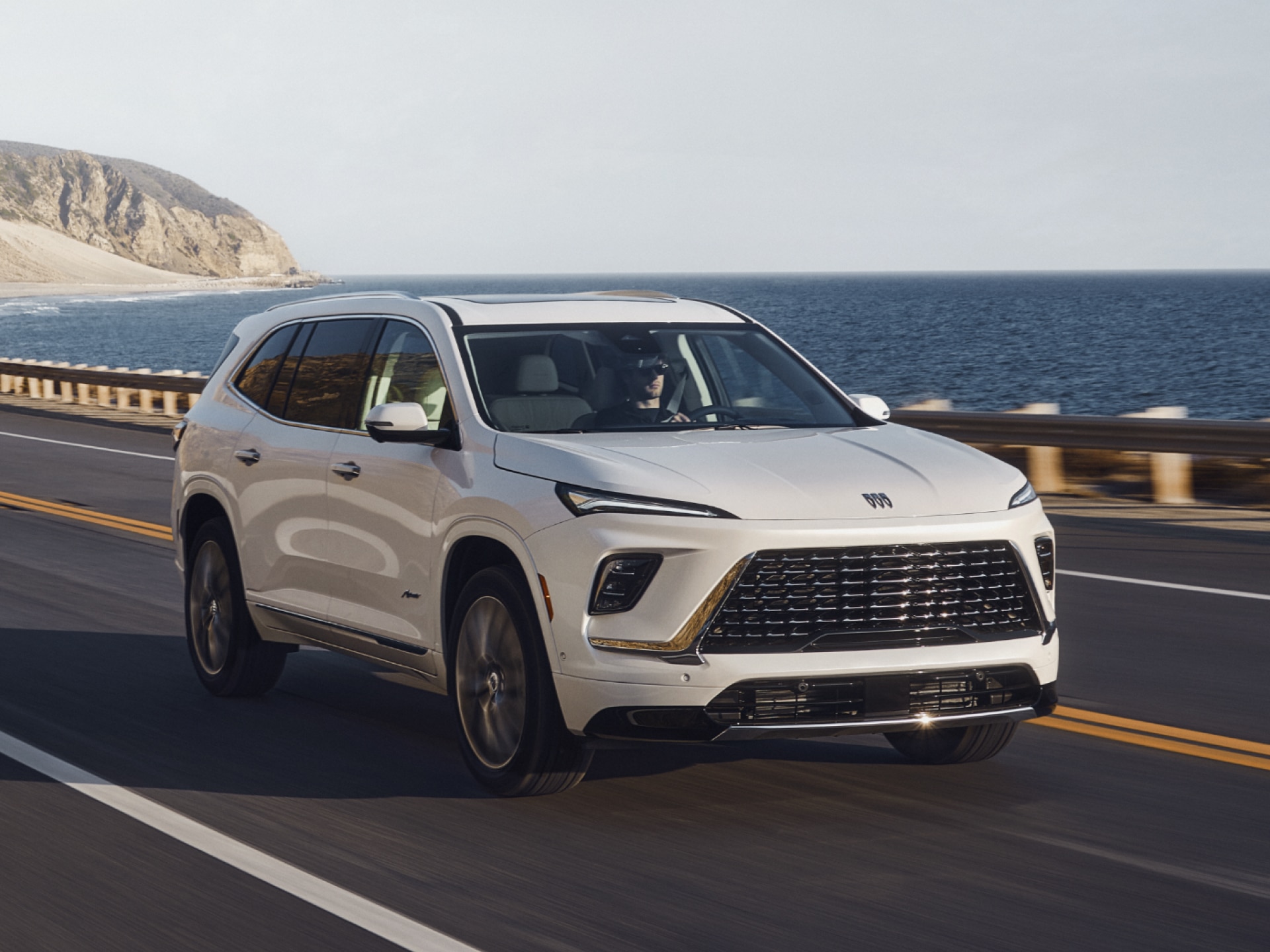 Front Three-Quarters View of a White Buick SUV Driving Down a Winding Mountain Road
