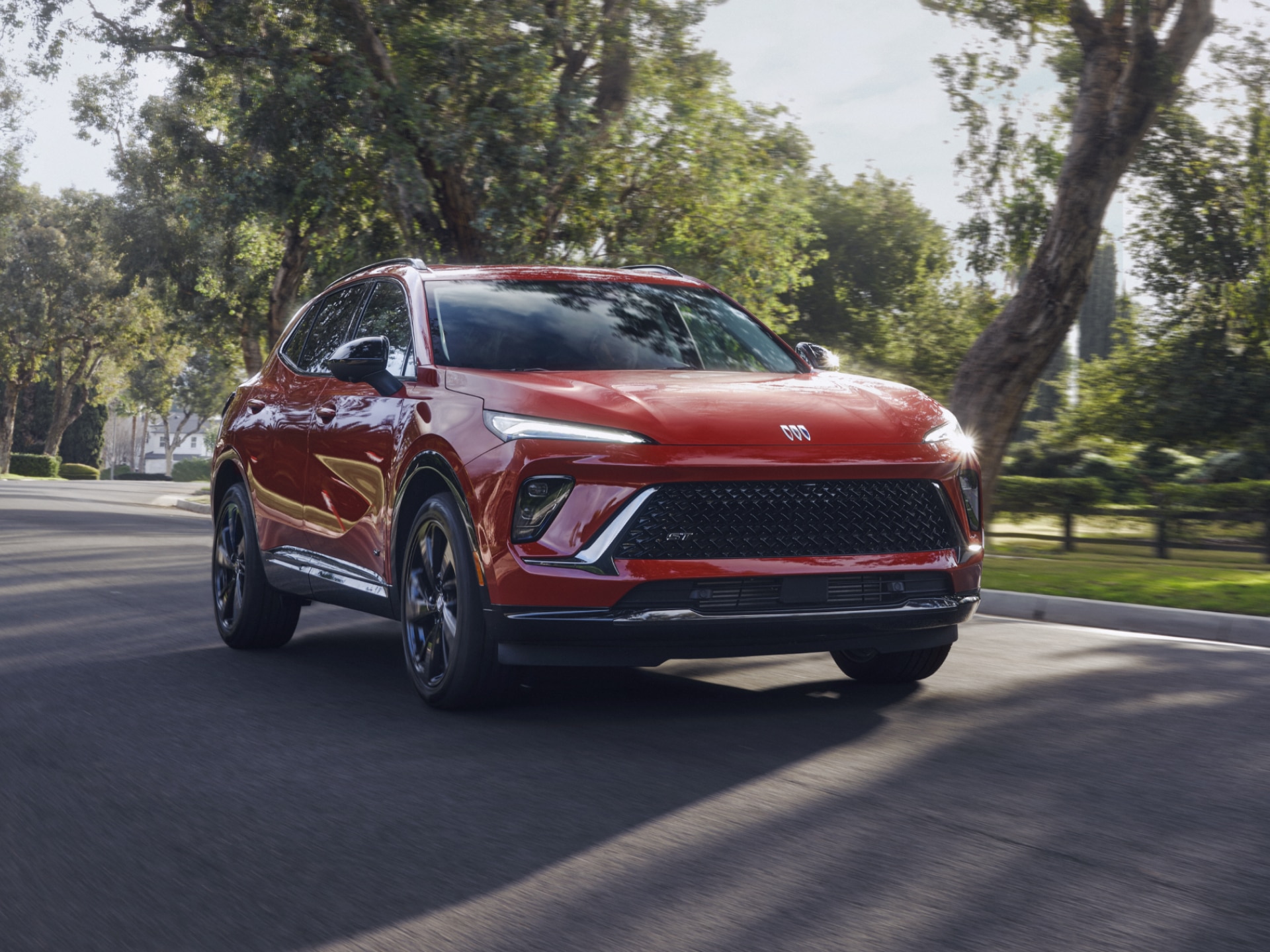 Front Three-Quarters View of a Red Buick SUV Driving Down a Neighborhood Street