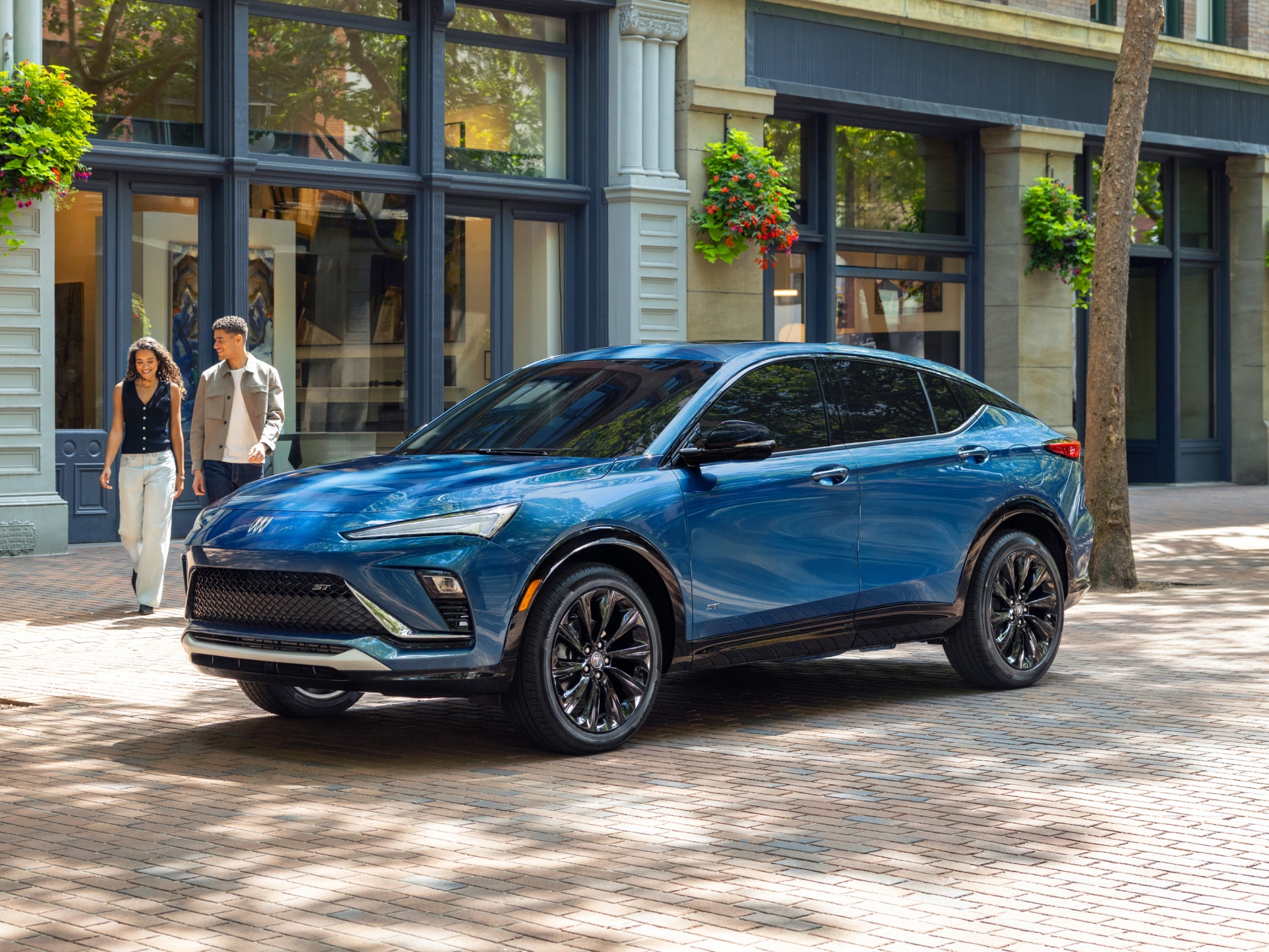 A Brilliant Blue Buick Envista ST SUV Parked on a Brick Sidewalk as Two People Walk Past a Storefront in the Background