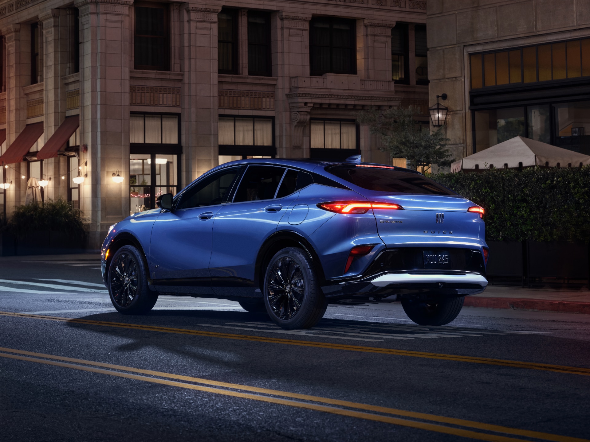 A Blue Buick SUV Parked on a City Street at Night with Taillights Illuminated and the Buick Logo Visible