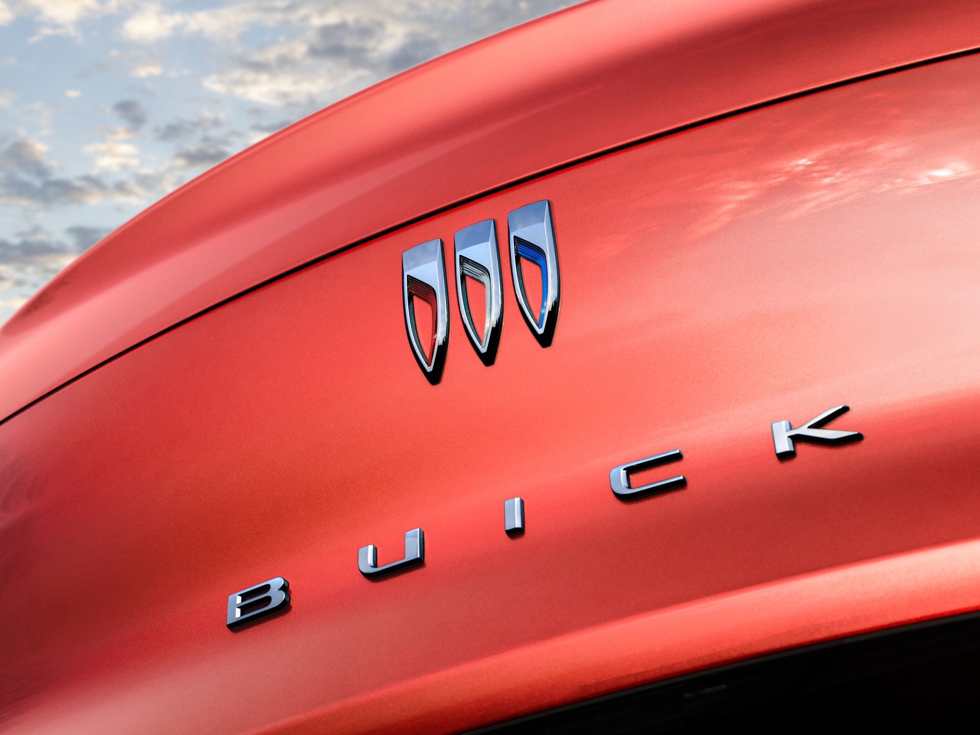 A Close-up View of the Chrome Buick Logo and a Wordmark on a Red Vehicle