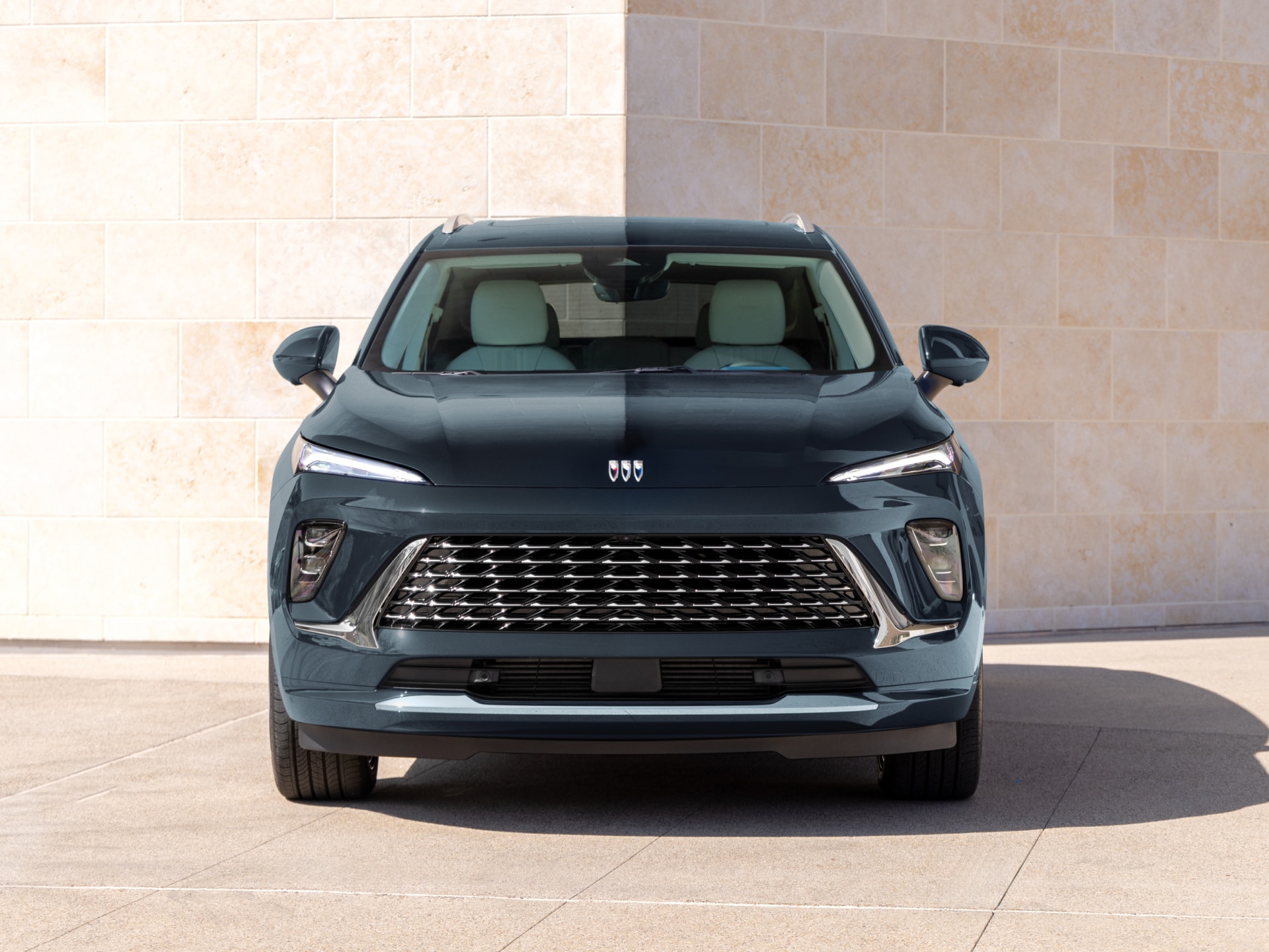 A Front View of a Dark Gray Buick SUV with a Distinctive Grille Parked by a Stone Wall