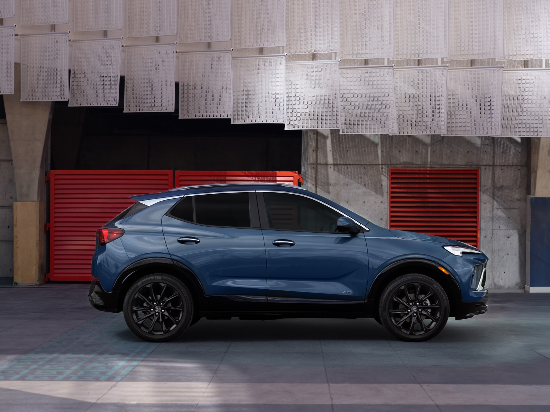 A Deep Blue Buick Crossover SUV with Black Wheels and Trim Parked in a Garage with Red Doors