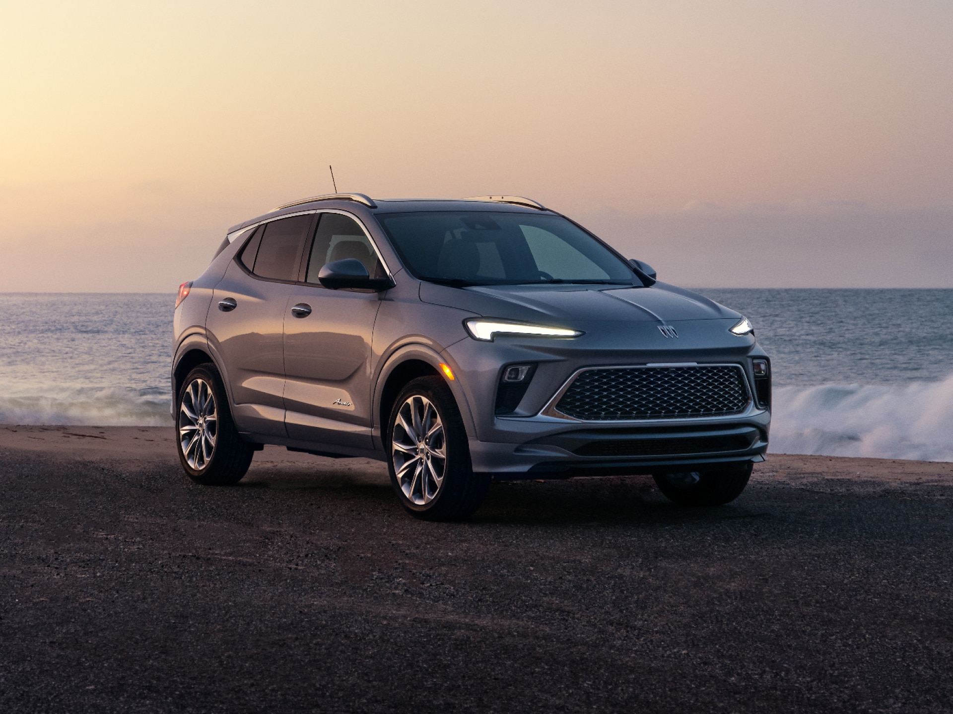 A Gray Buick Encore GX SUV Parked On The Asphalt Road By The Ocean At Sunset