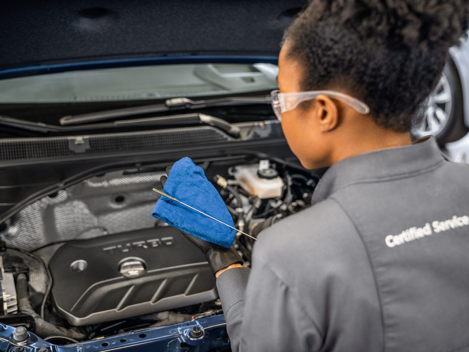 A Technician in Safety Glasses Checks the Oil in a Buick Engine with a Blue Cloth and Dipstick