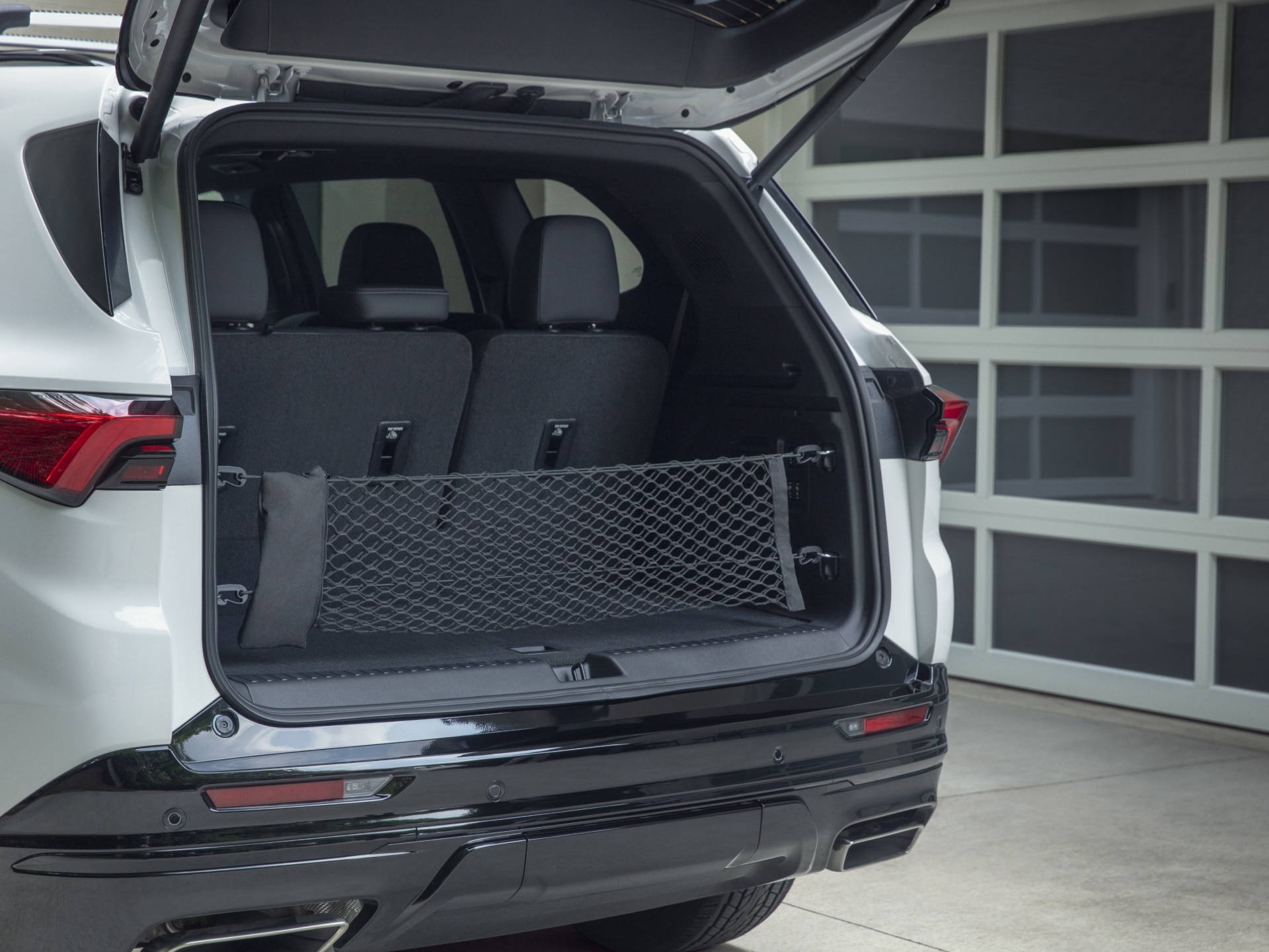 The Open Rear Cargo Area of a White Buick SUV with the Seats Folded Down and a Black Cargo Net Installed Against a White Garage Door