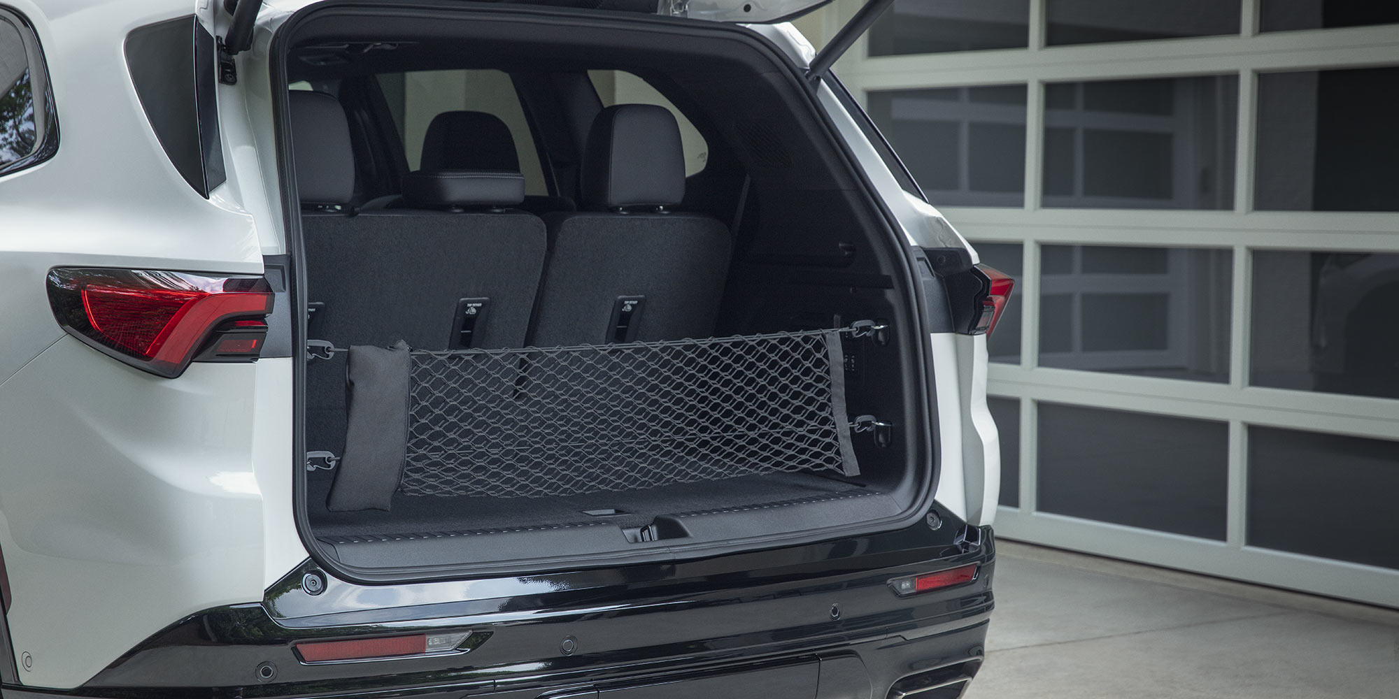 The Open Rear Cargo Area of a White Buick SUV with the Seats Folded Down and a Black Cargo Net Installed Against a White Garage Door