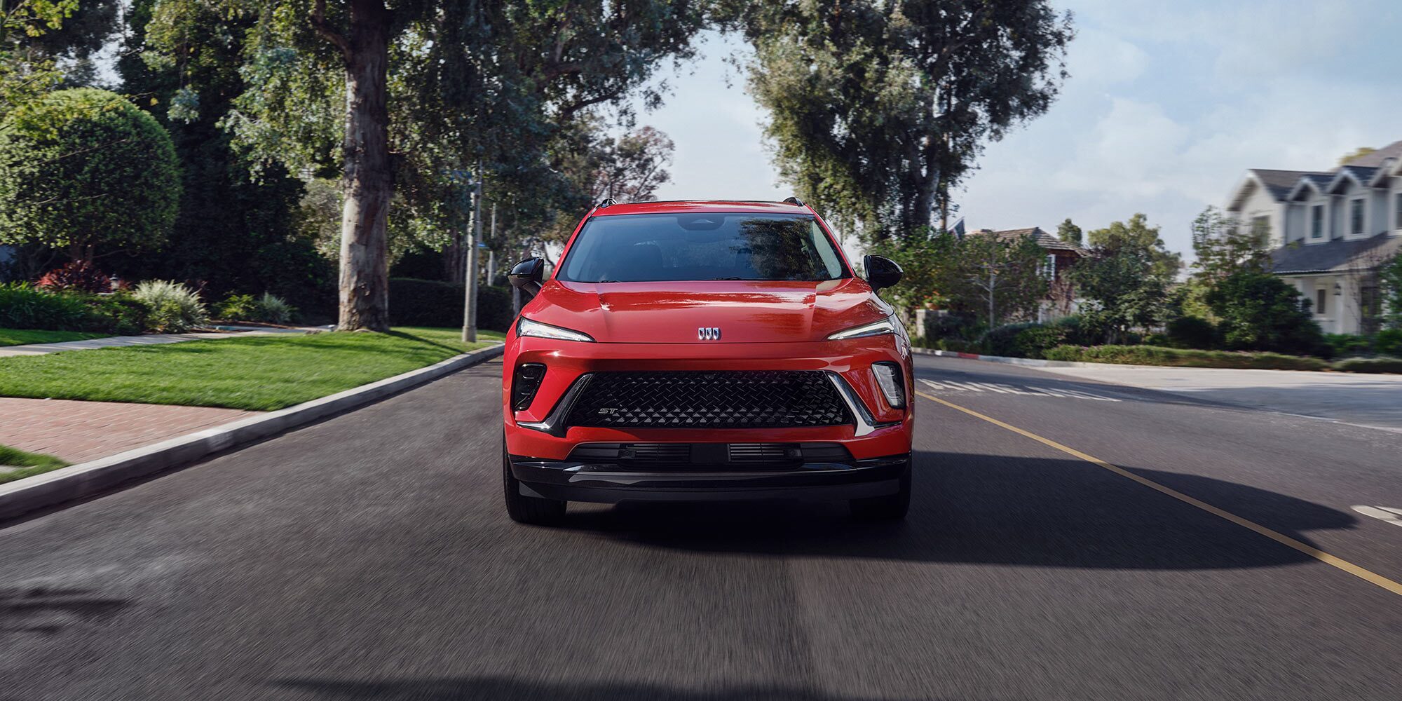 A Front View of a Bright Red Buick SUV Driving on a Tree Lined Street in a Suburban Neighborhood