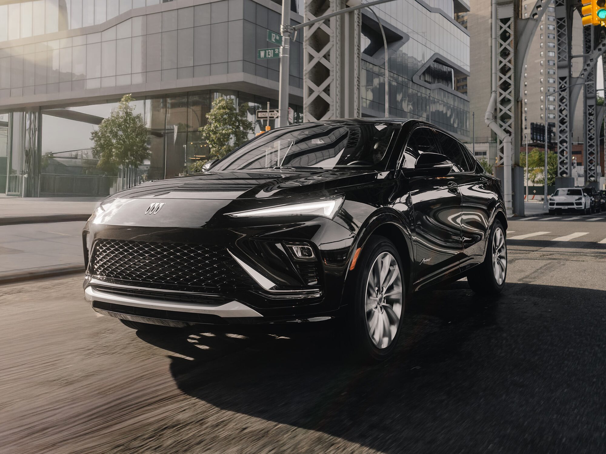 A Sleek Black Buick SUV Driving on a City Street with Modern Buildings and a Bridge in the Background